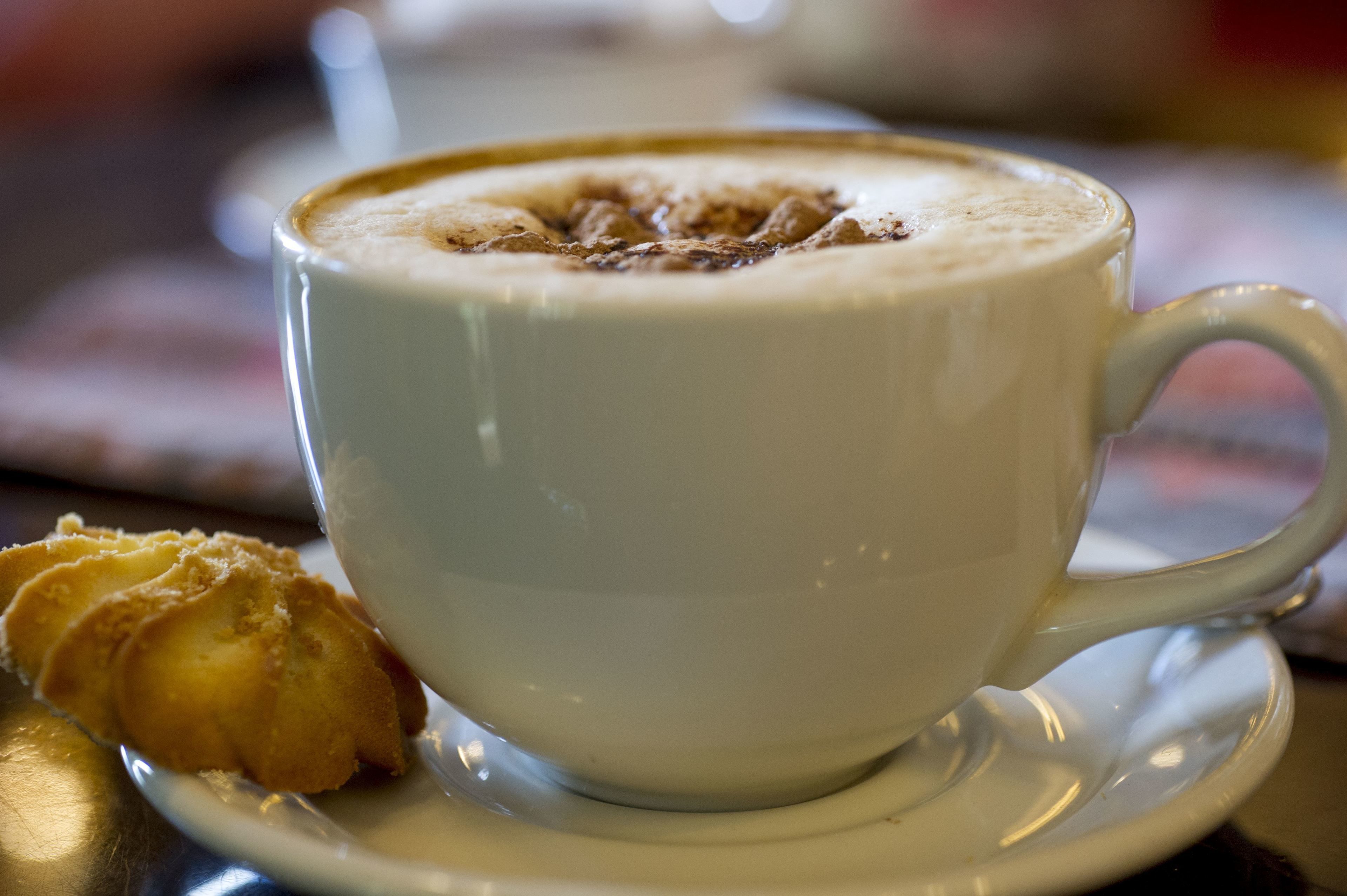 A cup of coffee with a frothy top and a pastry on a saucer.
