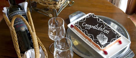 Une table avec une bouteille de vin, un panier de fruits, deux verres à vin et un gâteau pour célébrer l’événement.