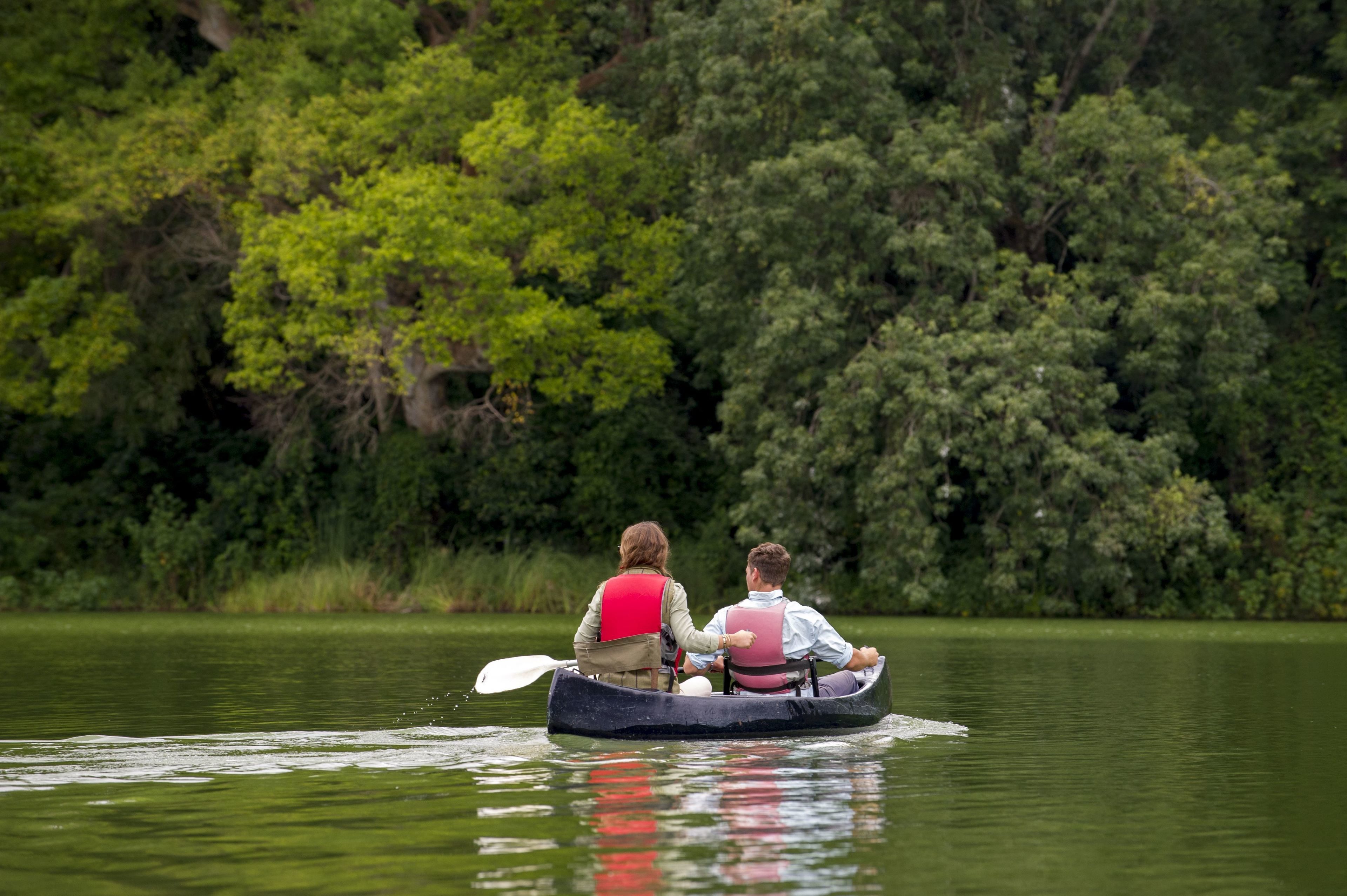 Two people in a canoe on a calm lake surrounded by dense greenery.