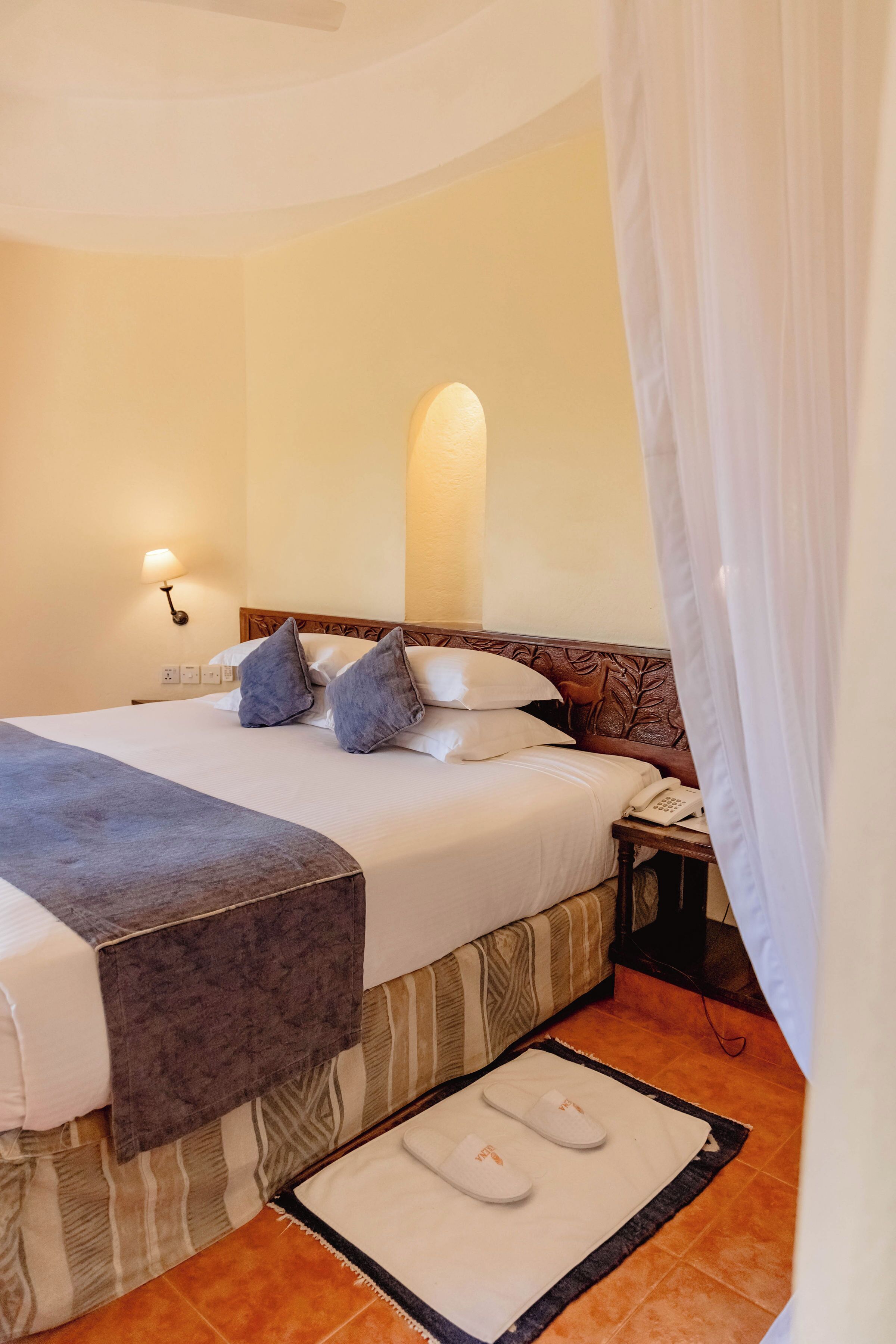 A hotel room with a bed, bedside table, lamp, and a telephone.