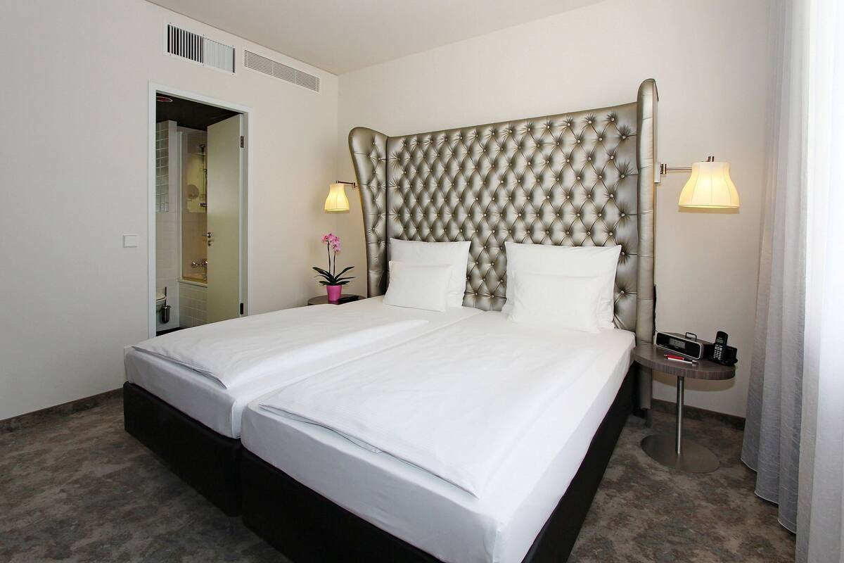 Una habitación de hotel con una cama grande, dos mesitas de noche, un espejo y una lámpara.
