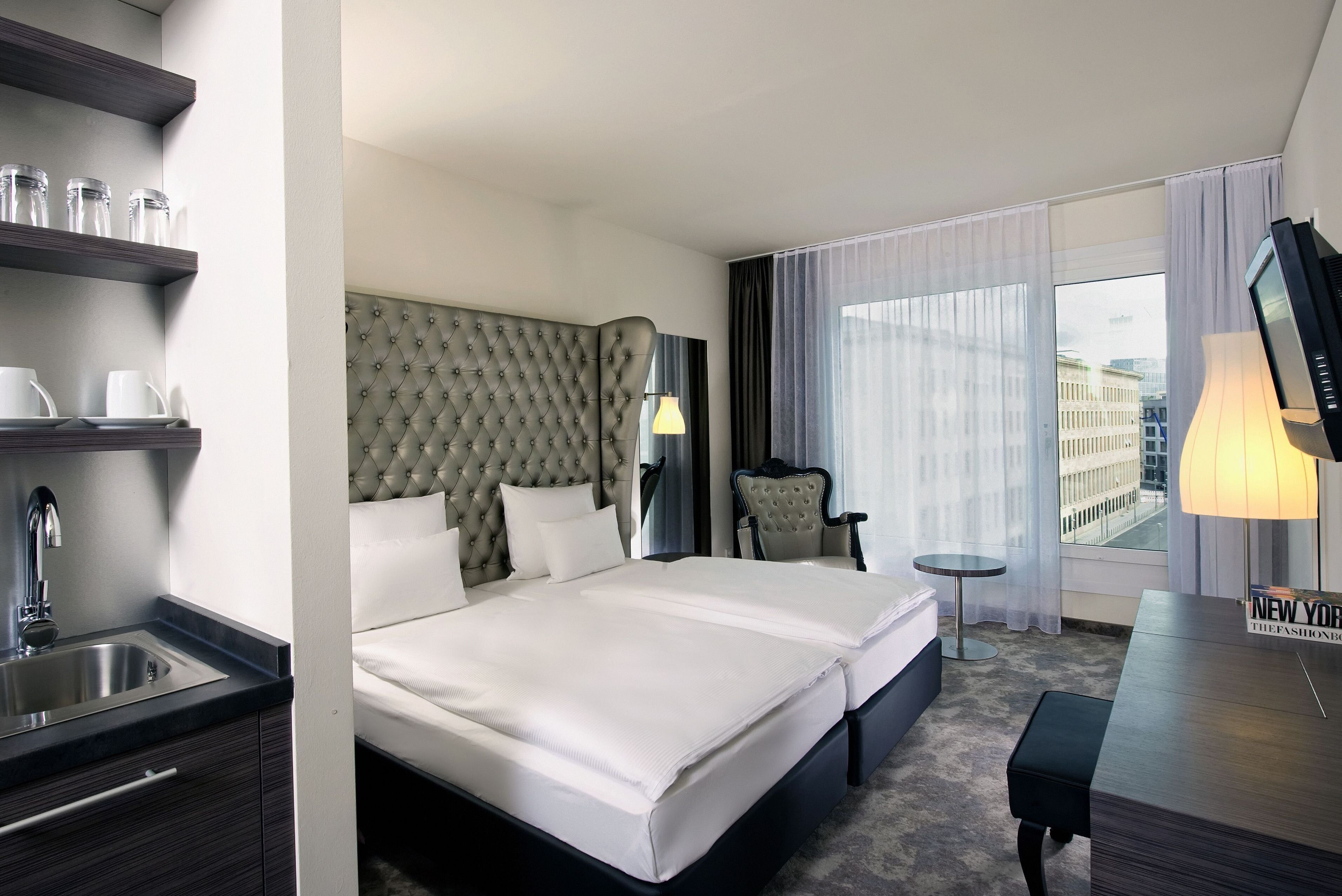 Ein Hotelzimmer mit einem großen Bett, einem Schreibtisch, einem Sessel, einem kleinen Tisch und Blick auf die Stadt.