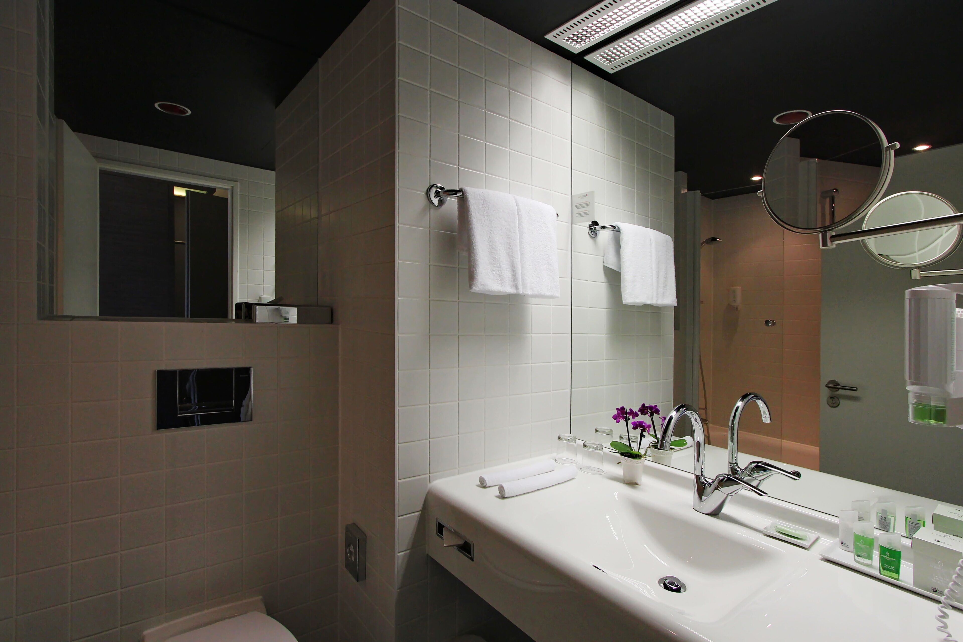 Un baño moderno con un lavamanos blanco, dos espejos y un perchero para toallas.