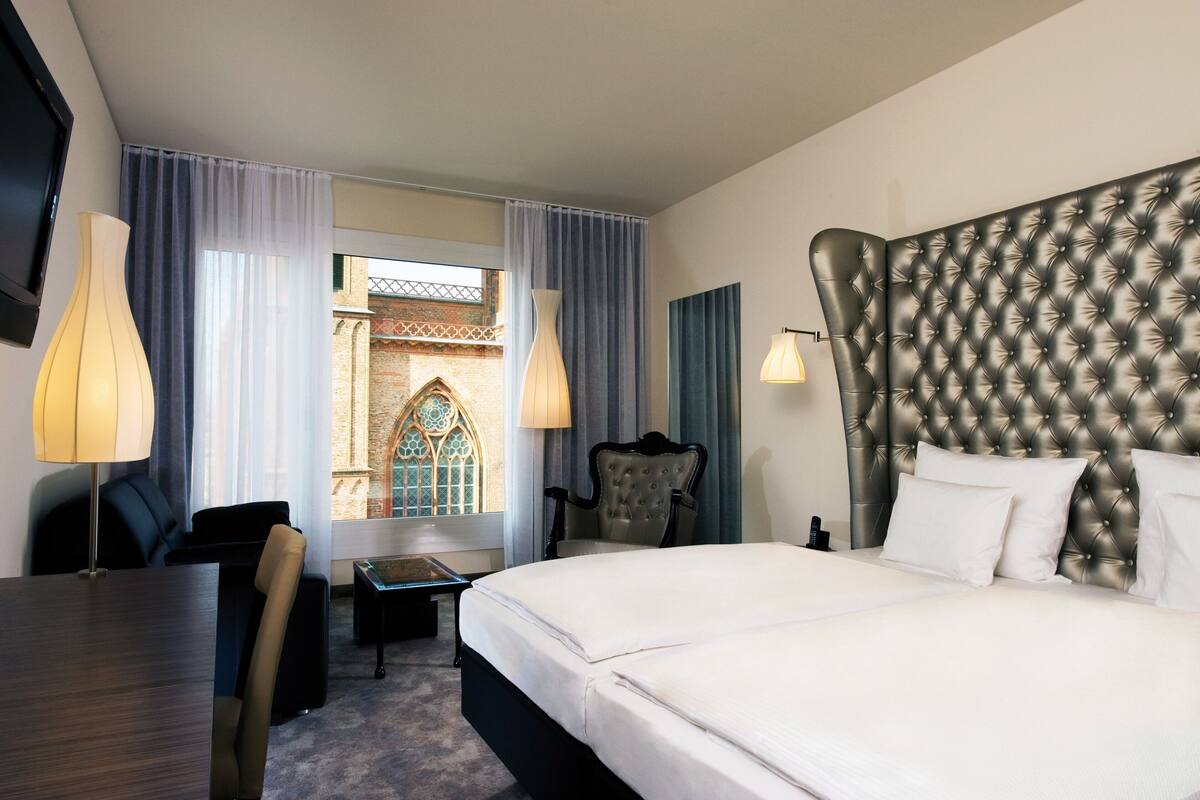 Habitación de hotel con una cama grande, un escritorio, una silla y vistas a un edificio con ventana.