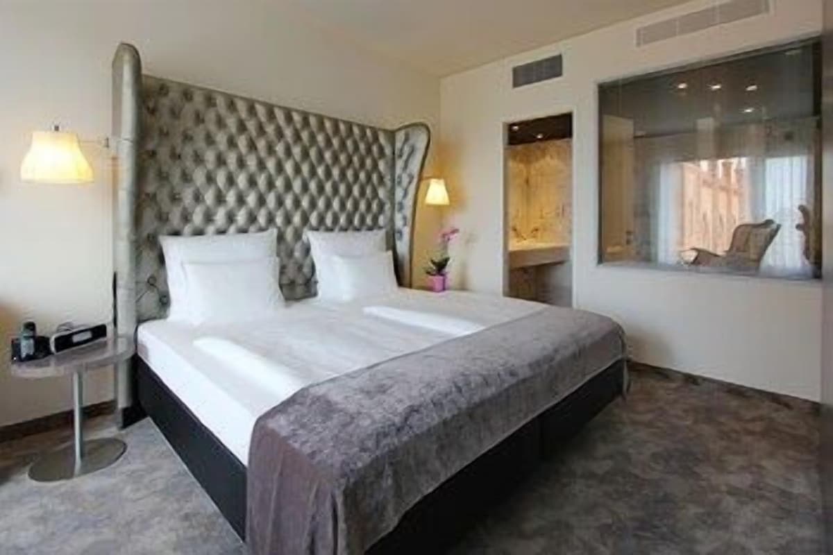 A hotel room with a large bed, a headboard, bedside tables, a window, and a mirror.