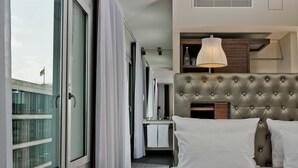 Habitación de hotel con una cama grande, cabecero, escritorio y ventana con cortinas.