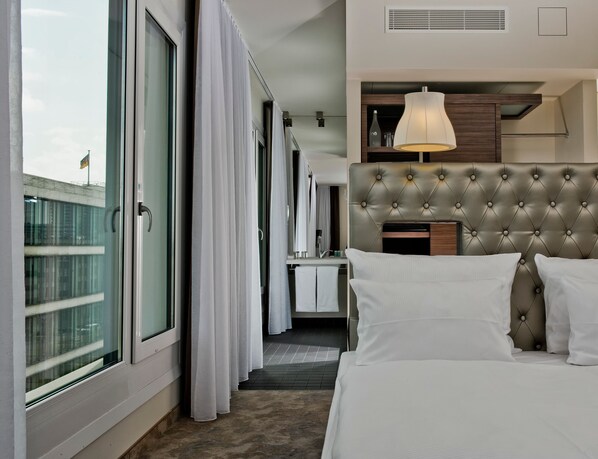 A hotel room with a large bed, a headboard, a desk, and a window with curtains.