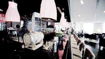 A bar area with a long counter, multiple stools, and hanging pink pendant lights.