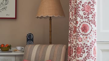 Una silla con estampado a rayas, un cojín rojo, una lámpara, una obra de arte enmarcada y una cortina estampada.