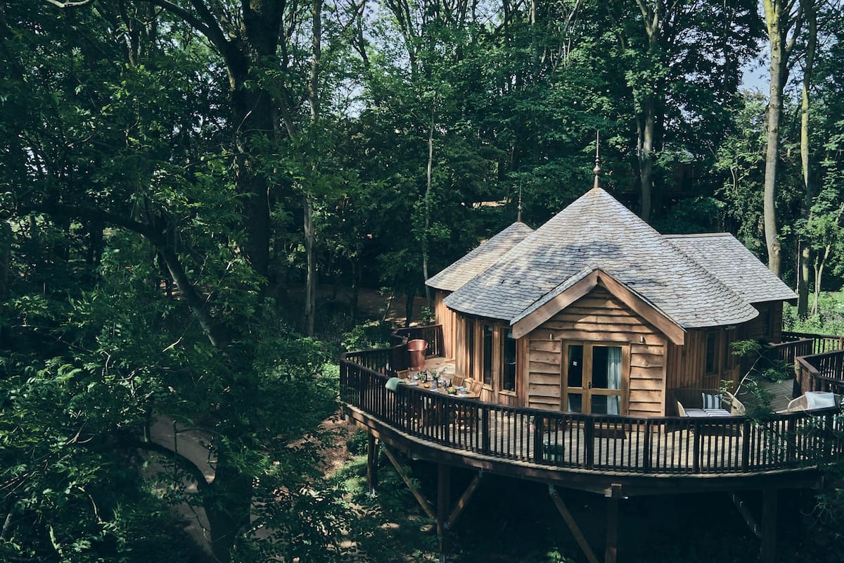 Ein hölzernes Baumhaus mit geneigtem Dach, umgeben von dichtem Wald.