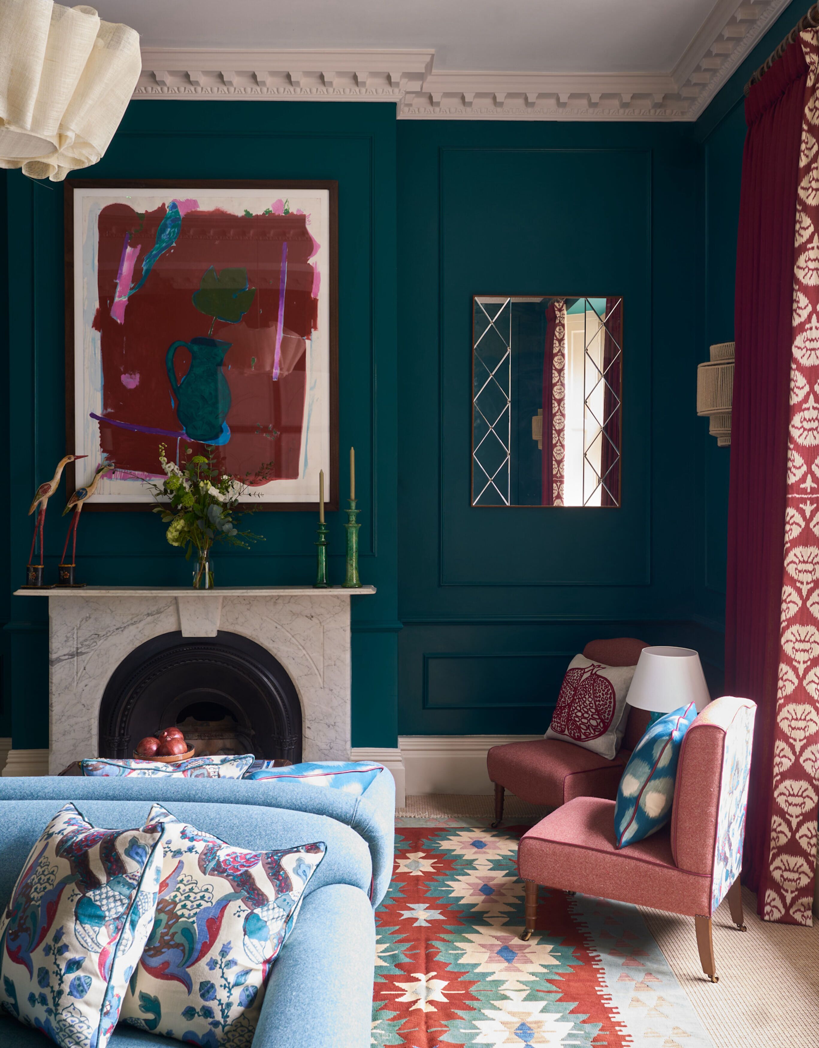 A teal-colored room with a fireplace, a large abstract painting, a mirror, and a patterned rug.
