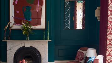 A teal-colored room with a fireplace, a large abstract painting, a mirror, and a patterned rug.