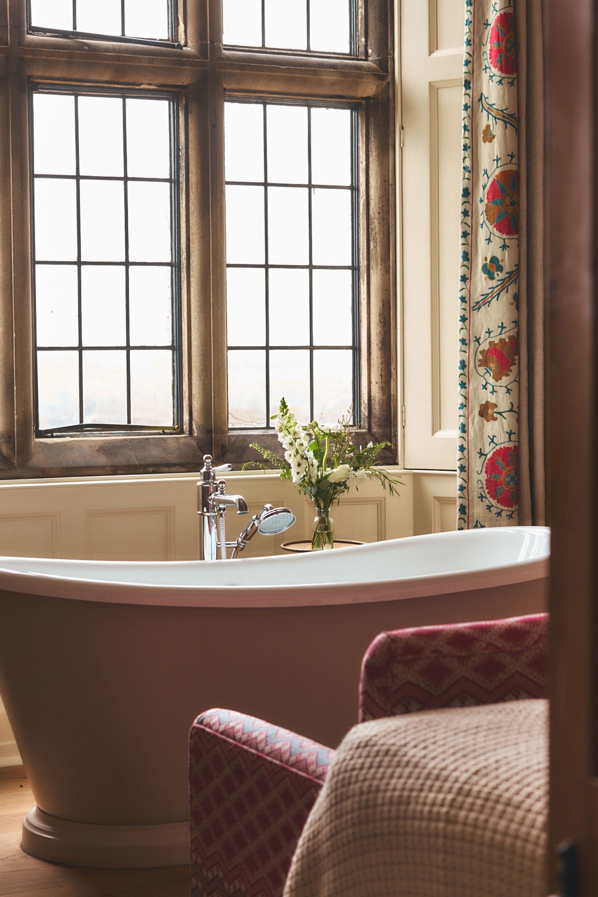 Un baño con una bañera independiente, un ventanal con diseño de celosía y una cortina con motivos florales.