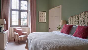 Un dormitorio con una cama grande, una silla, una ventana con cortinas, una puerta y un cuadro en la pared.