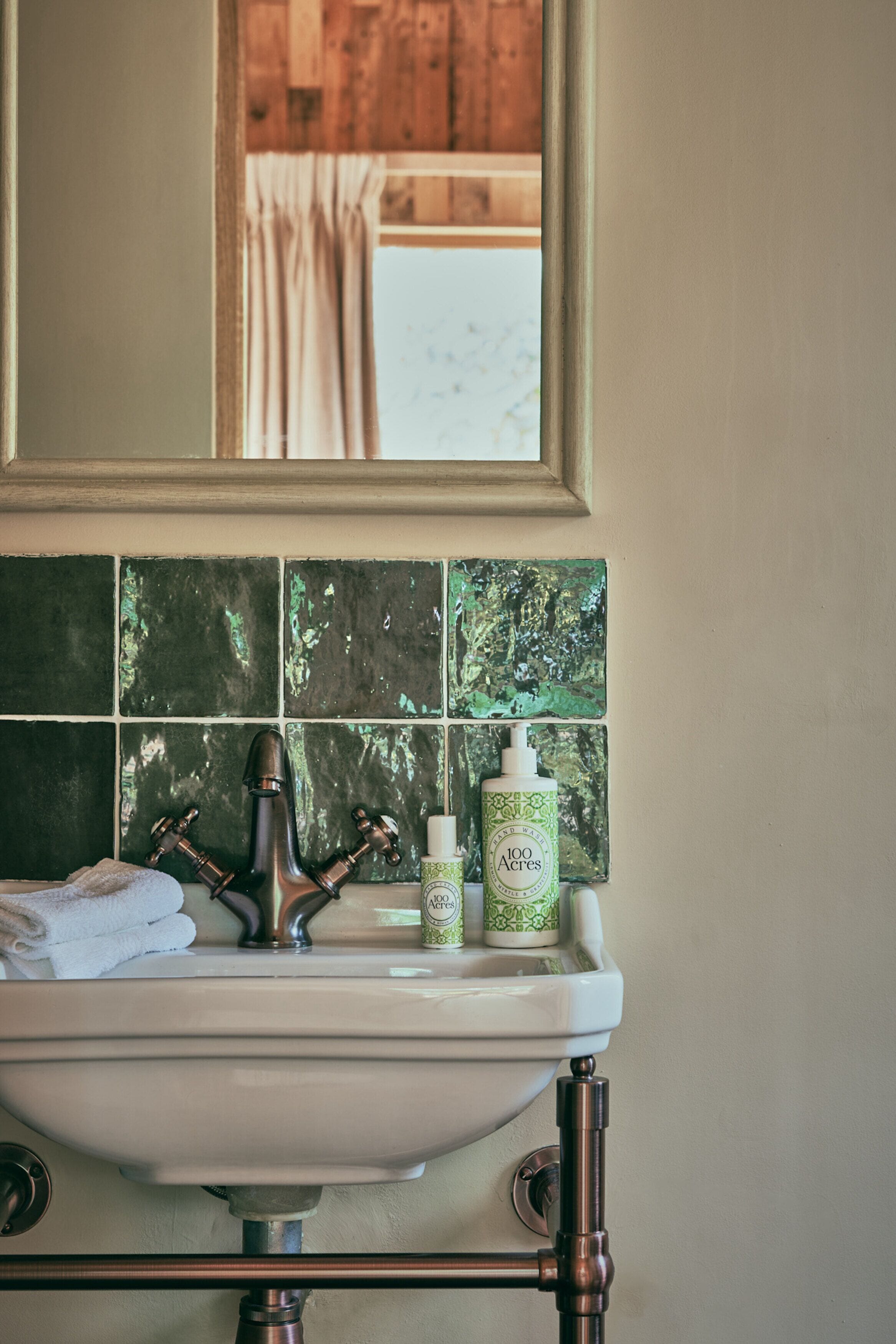 A bathroom sink with a mirror above it, a window with curtains, and a green tiled backsplash.