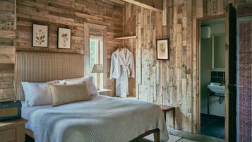 A wooden cabin bedroom with a bed, a nightstand, a robe, and framed botanical prints on the wall.