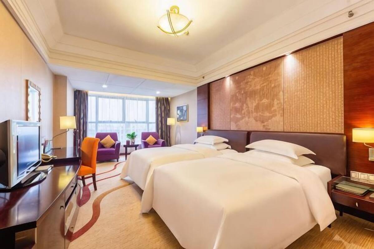 Habitación de hotel con dos camas, un escritorio con televisor, una silla y una ventana con cortinas.
