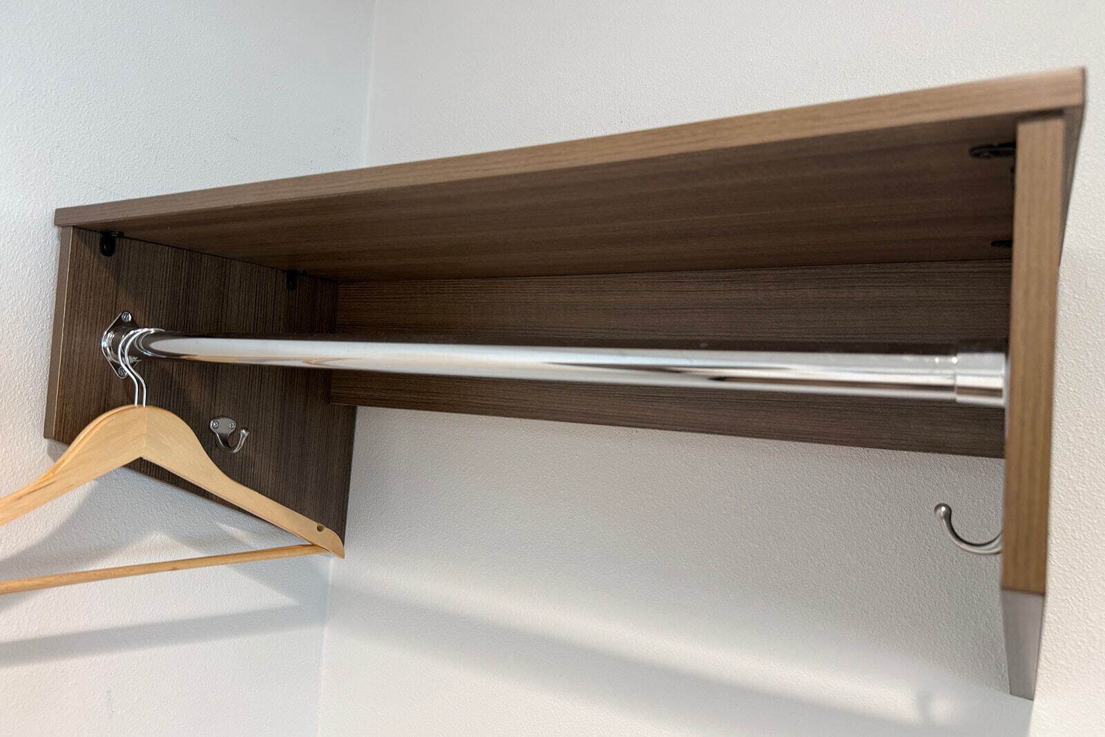 Una estantería de madera con una barra de metal, un perchero de madera y un gancho en la pared.