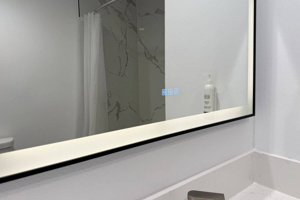 Een badkamer met een grote spiegel, een marmeren wand en een fles handzeep.