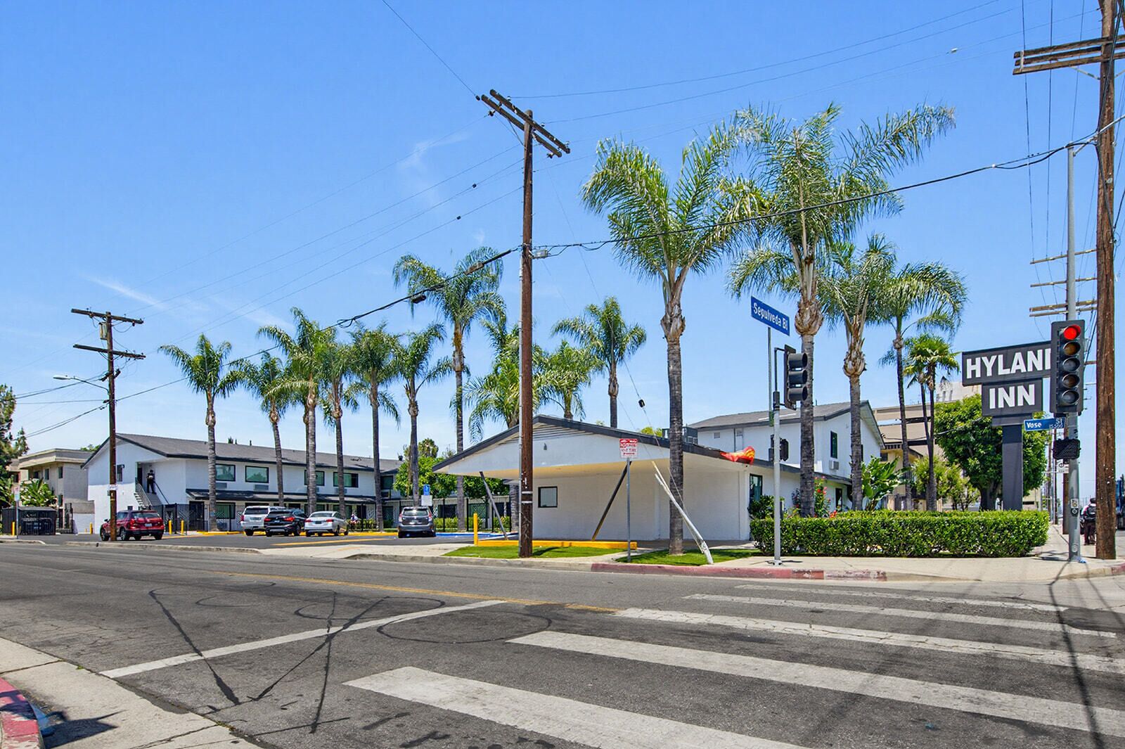 A street view with a hotel named 'HYLANI INN' at an intersection, palm trees, and a crosswalk.