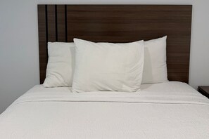 A bed with a wooden headboard, white bedding, and two pillows. - Hyland Motel Van Nuys (Van Nuys)