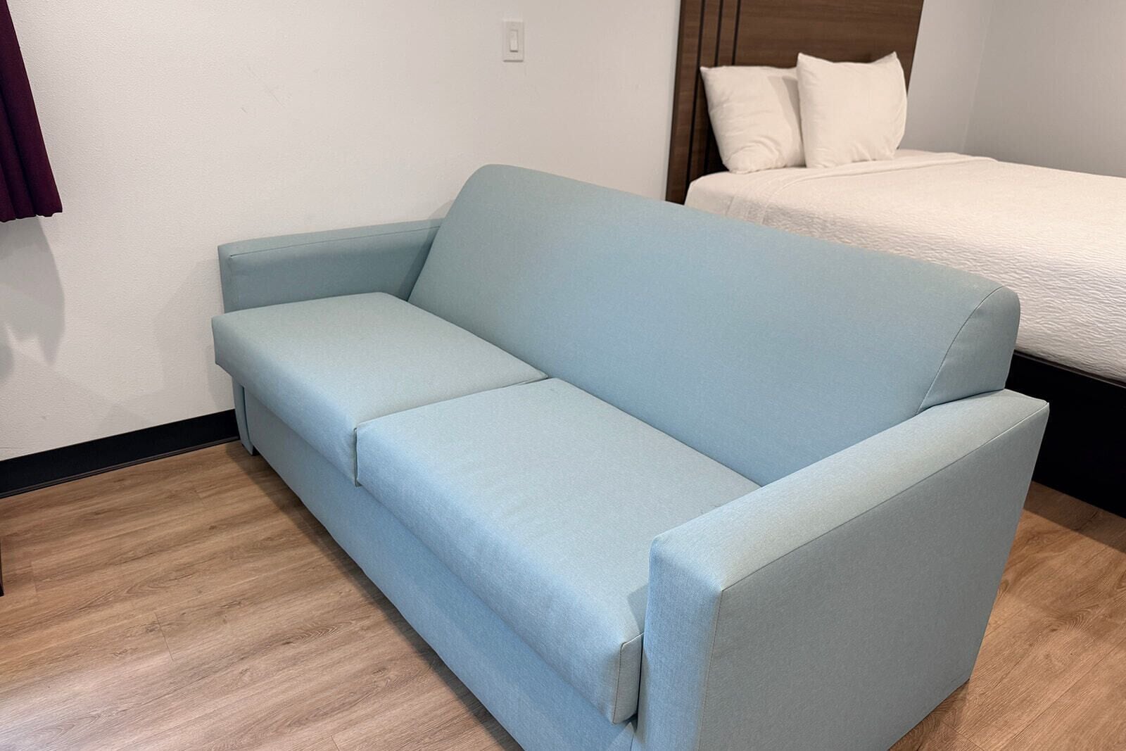 A light blue sofa in a room with a wooden floor and a bed with white bedding.