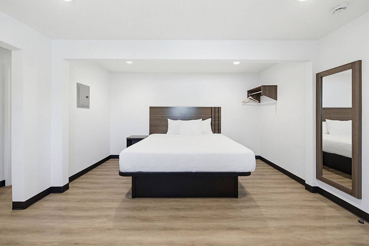 Een hotelkamer met een groot bed, nachtkastje, kledingkast en spiegel.