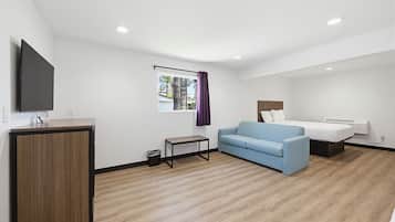 Ein Hotelzimmer mit einem Bett, einem blauen Sofa, einem kleinen Tisch, einem an einer Kommode befestigten Fernseher und einem Fenster mit Vorhängen.
