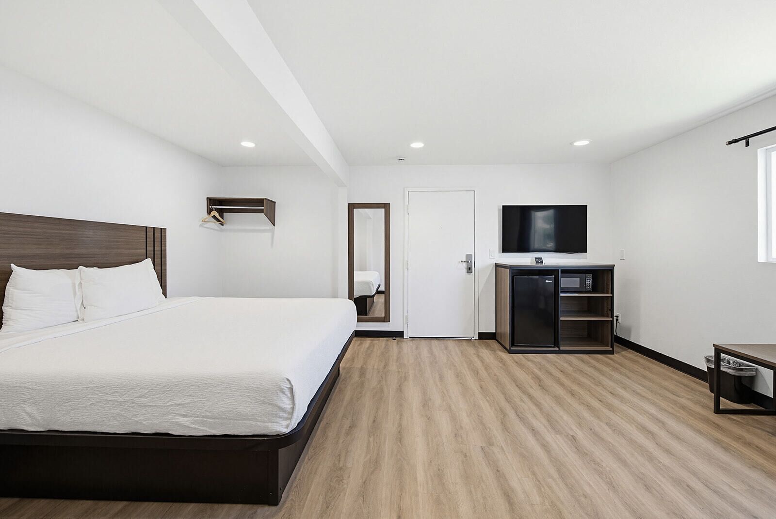 A hotel room with a bed, a TV, a mini-fridge, a coat rack, and a door.