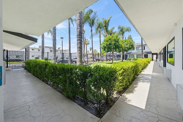 A modern building with a geometric design, a paved walkway, and a well-maintained garden with palm trees.