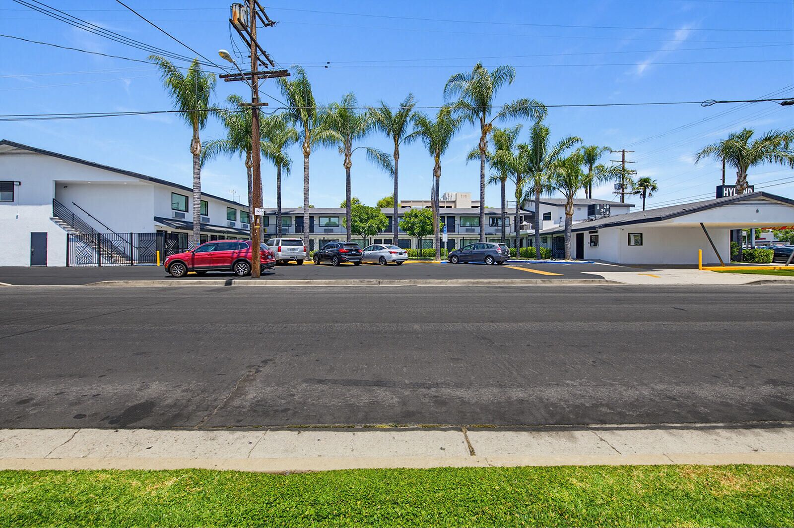 A street view with parked cars, palm trees, and buildings with a sign reading 'HYL MD'.
