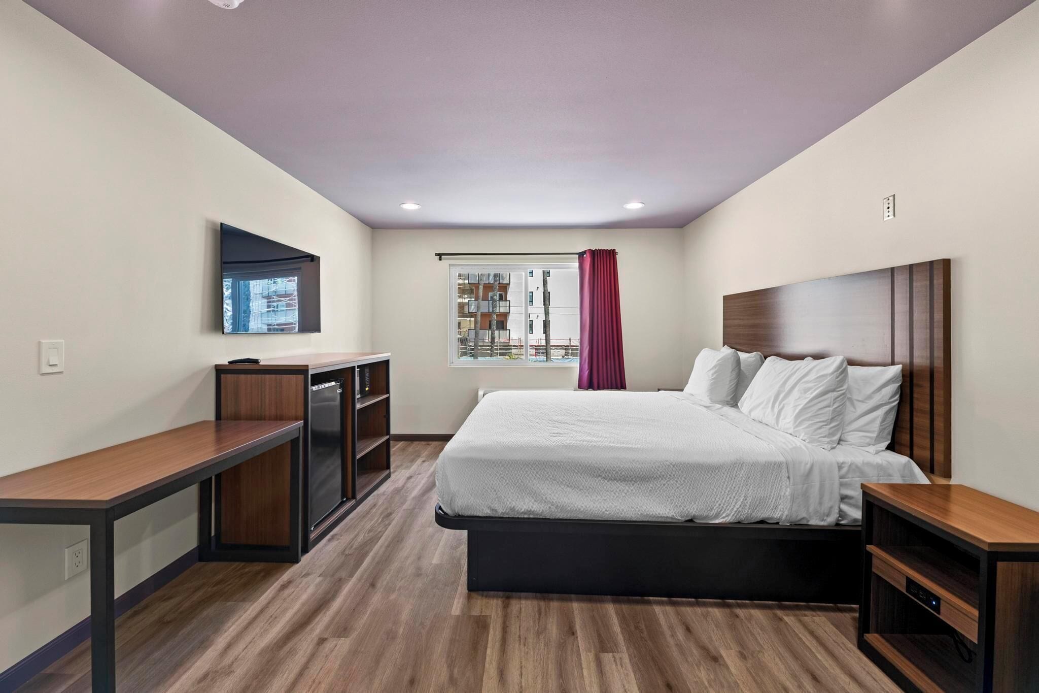 A modern hotel room with a large bed, a desk, and a TV on the wall.