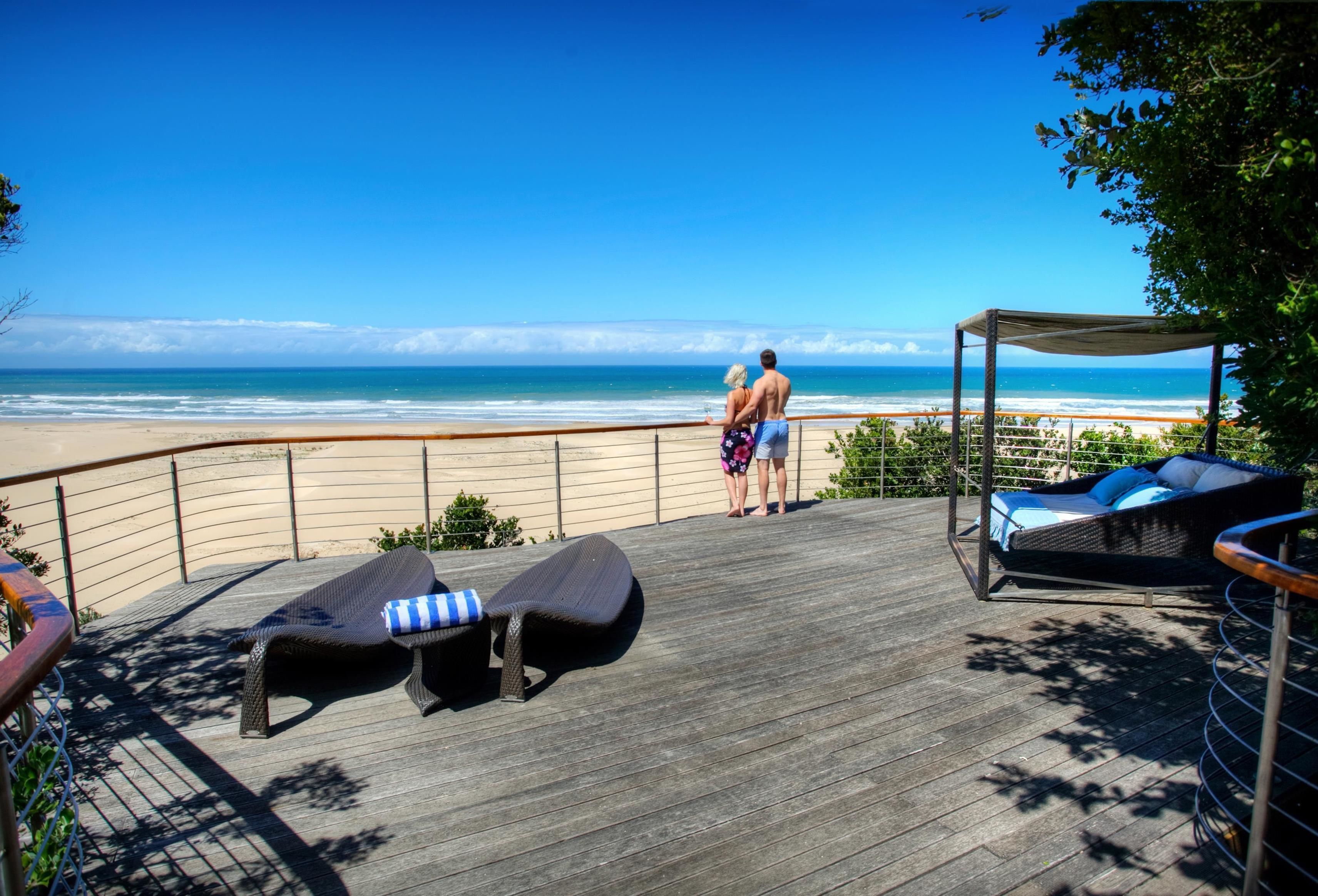 A wooden deck with lounge chairs and a canopy overlooking a beach.