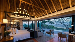 A bedroom with a large bed, a sitting area with a table, and a view of the outdoors.