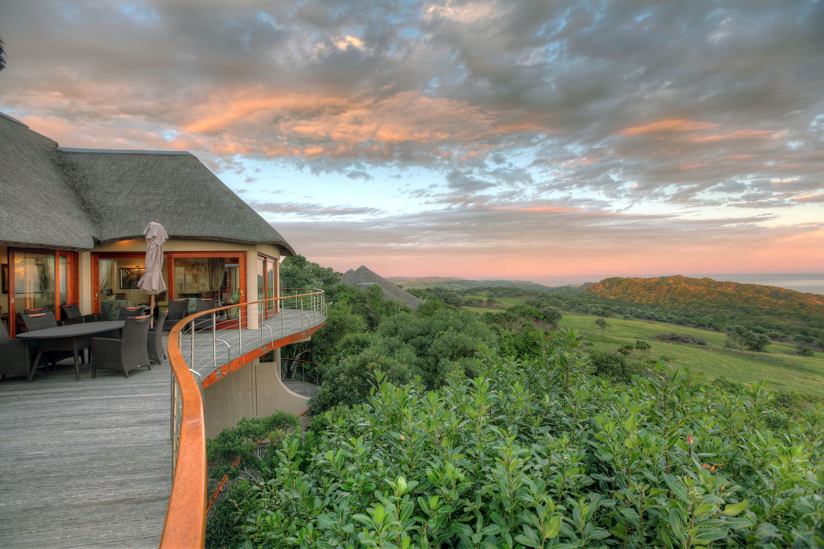 A thatched-roof building with outdoor seating and a scenic view of hills.