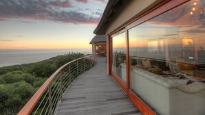 A balcony with a view of the ocean, a seating area with cushions, and a glass door leading to the interior.