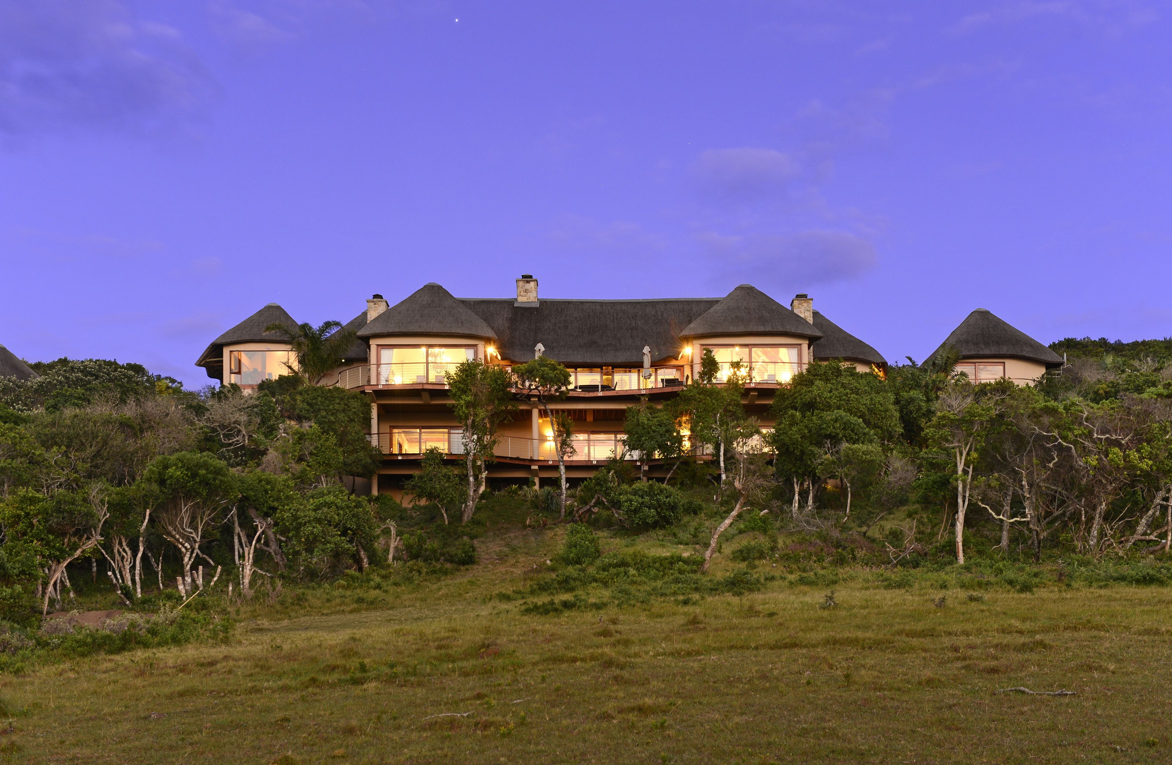 A large, multi-story building with a thatched roof, surrounded by lush greenery.