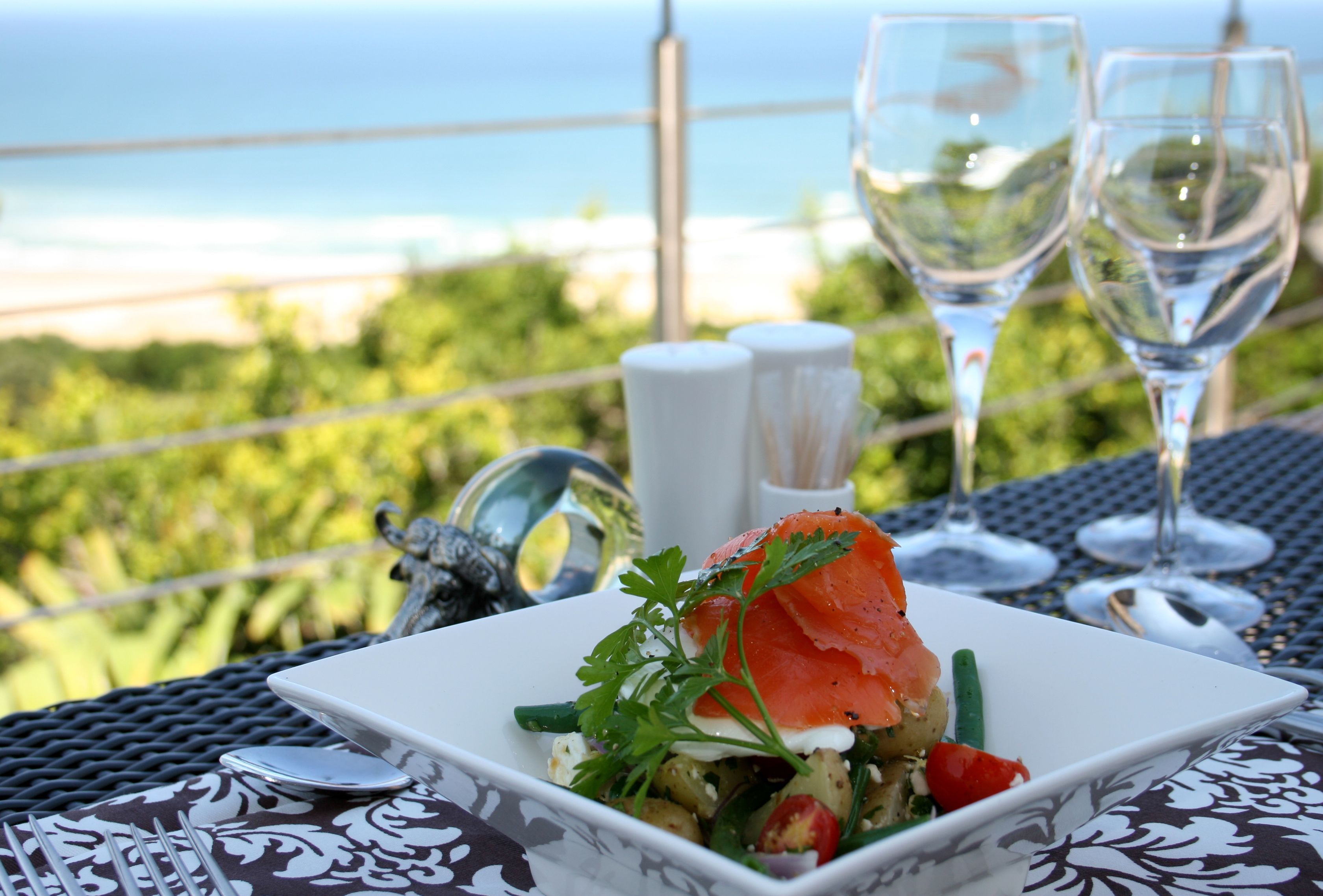 A table with a meal, two glasses of water, and a view of the ocean.