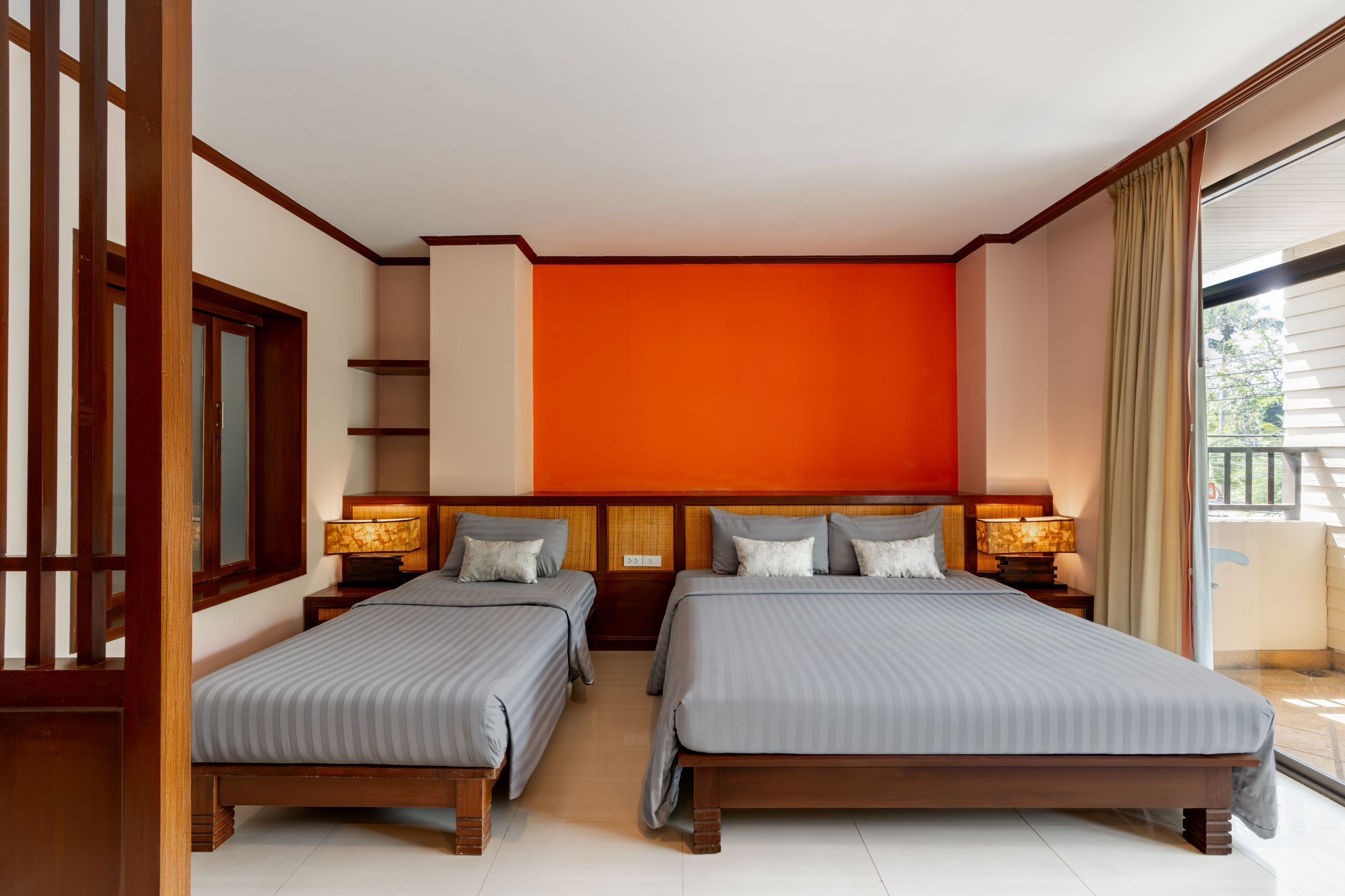 A hotel room with two beds, wooden headboards, and a bright orange accent wall.