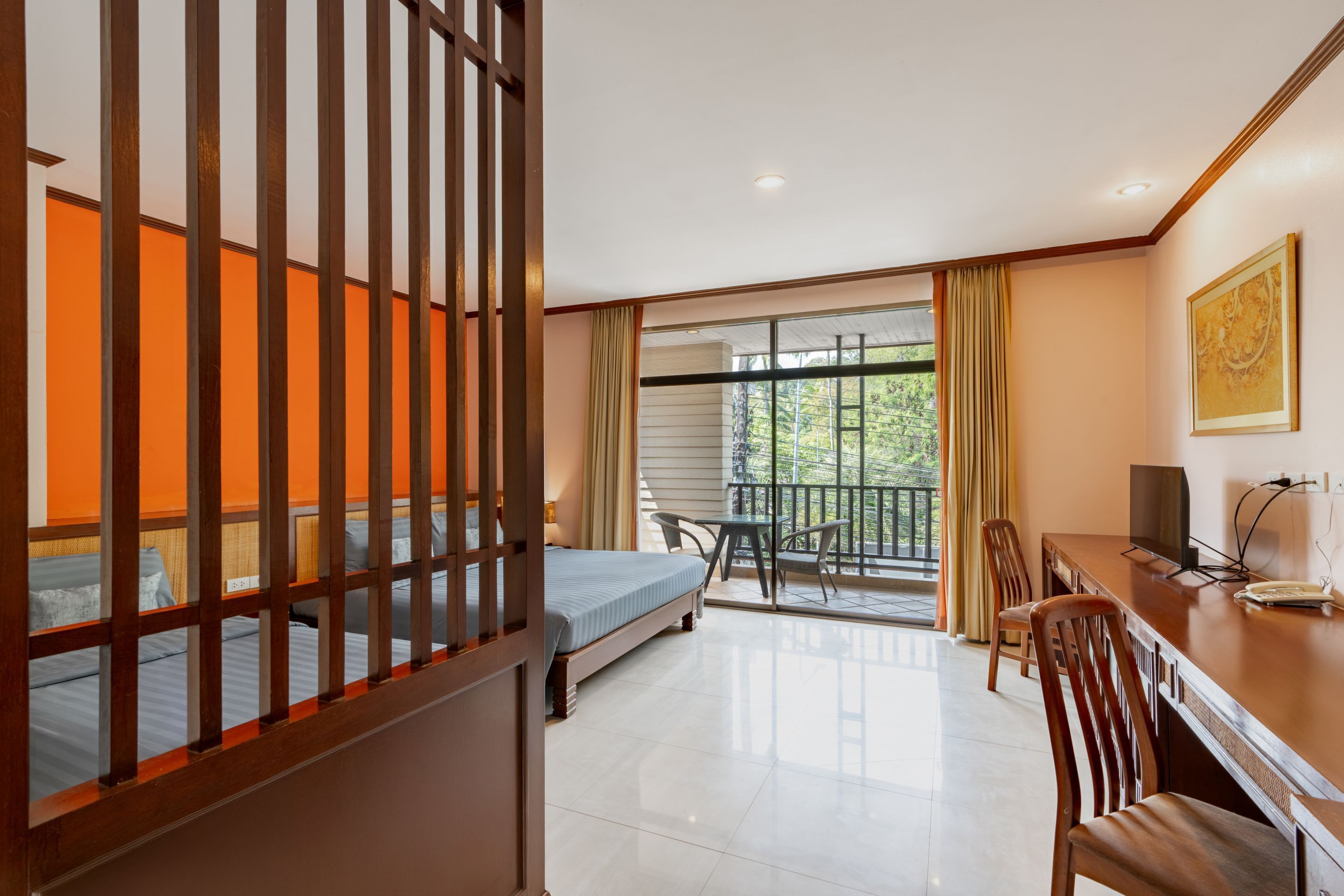 Une chambre d’hôtel avec un lit, un bureau, une chaise, une télévision et un balcon donnant sur la verdure.