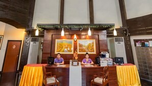 Un comptoir d’accueil avec deux employés, des poutres en bois et un luminaire au plafond.