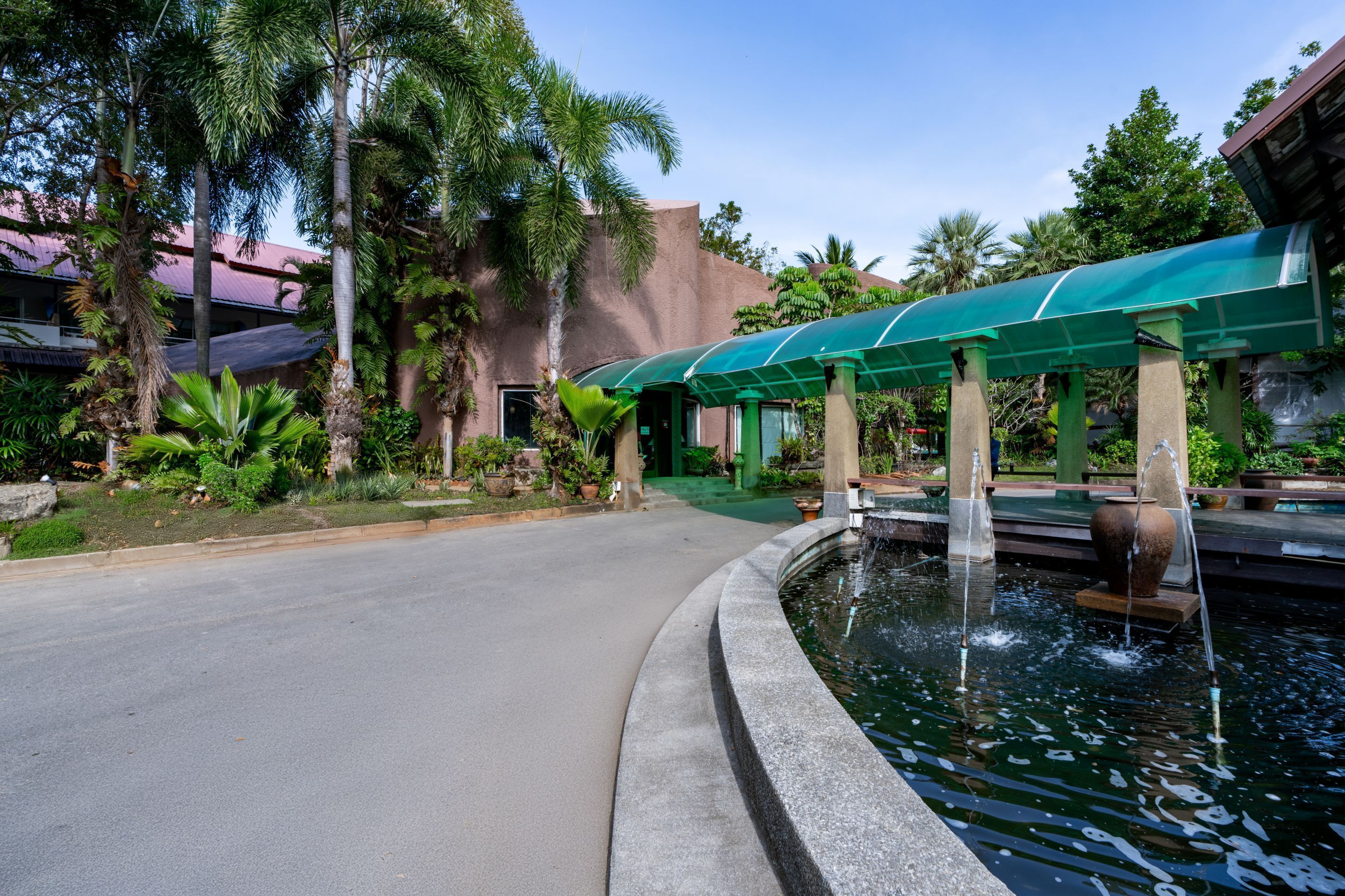 A paved pathway leading to a covered seating area with a water feature.
