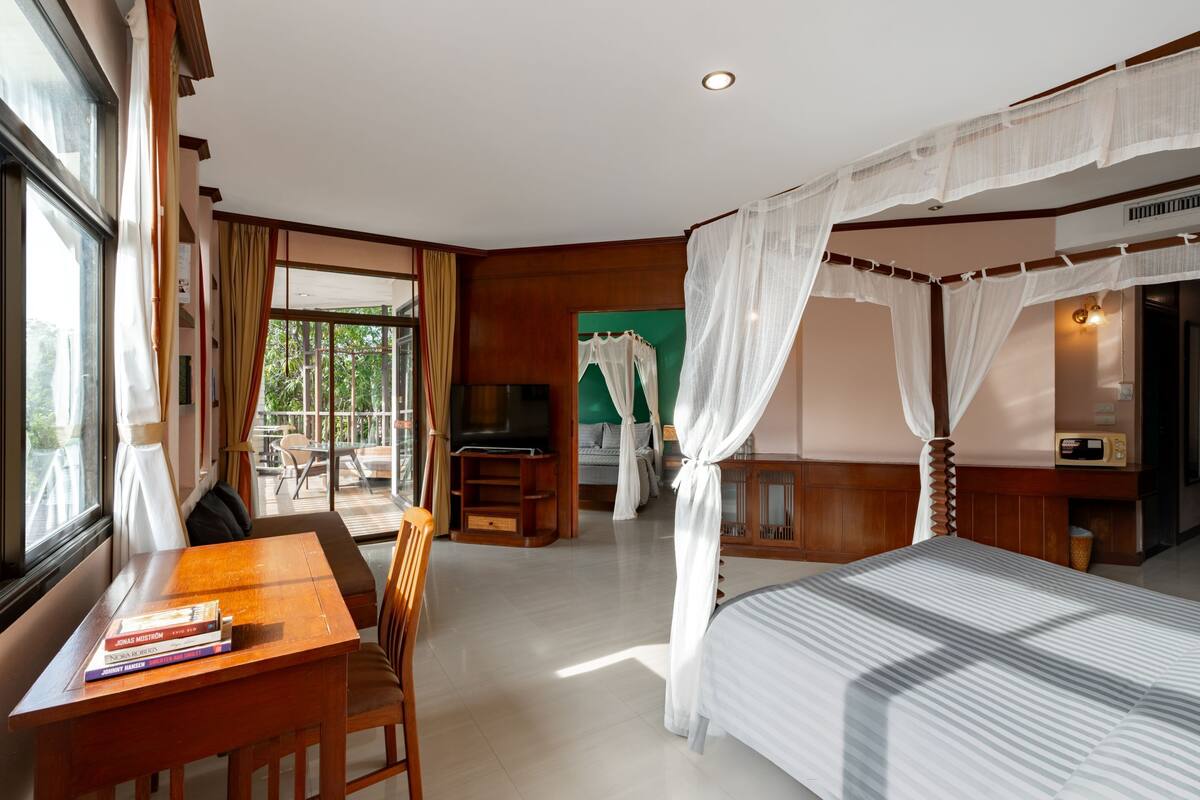 A hotel room with a bed, a TV, a desk with books, and a view of the outdoors.