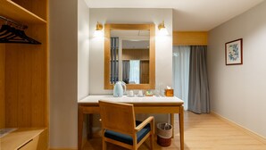 Une chambre d’hôtel avec un bureau en bois, une chaise, un miroir, une petite table, un panier et une armoire.