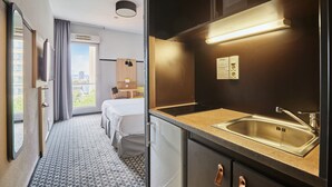 Una habitación de hotel con una cama, una kitchenette pequeña con un lavamanos y un ventanal con vista a la ciudad.