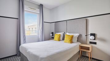 Een hotelkamer met een groot bed, twee nachtkastjes, een wandlamp en een raam met gordijnen.