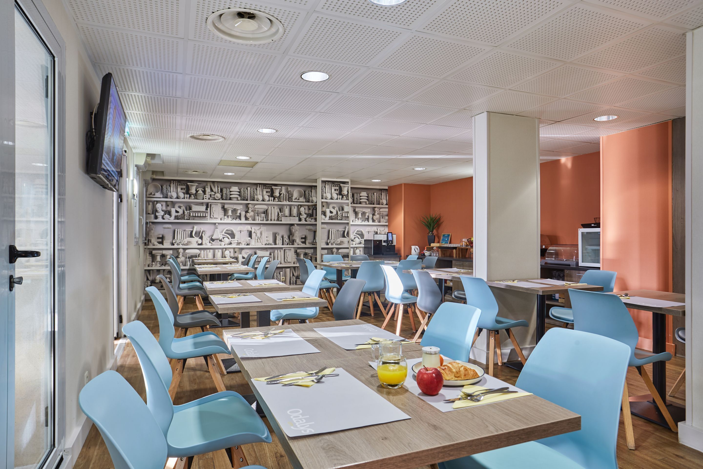Een moderne eetruimte met blauwe stoelen, houten tafels en een wand vol zwart-witfoto’s.