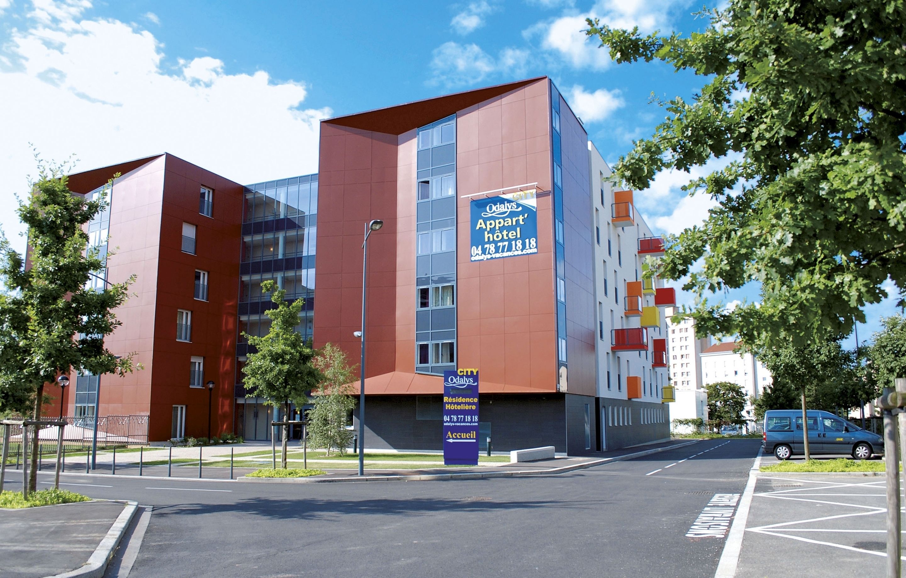 Un bâtiment moderne, avec une enseigne indiquant « Odalis Appart », qui se distingue par sa façade rouge et ses nombreuses fenêtres.