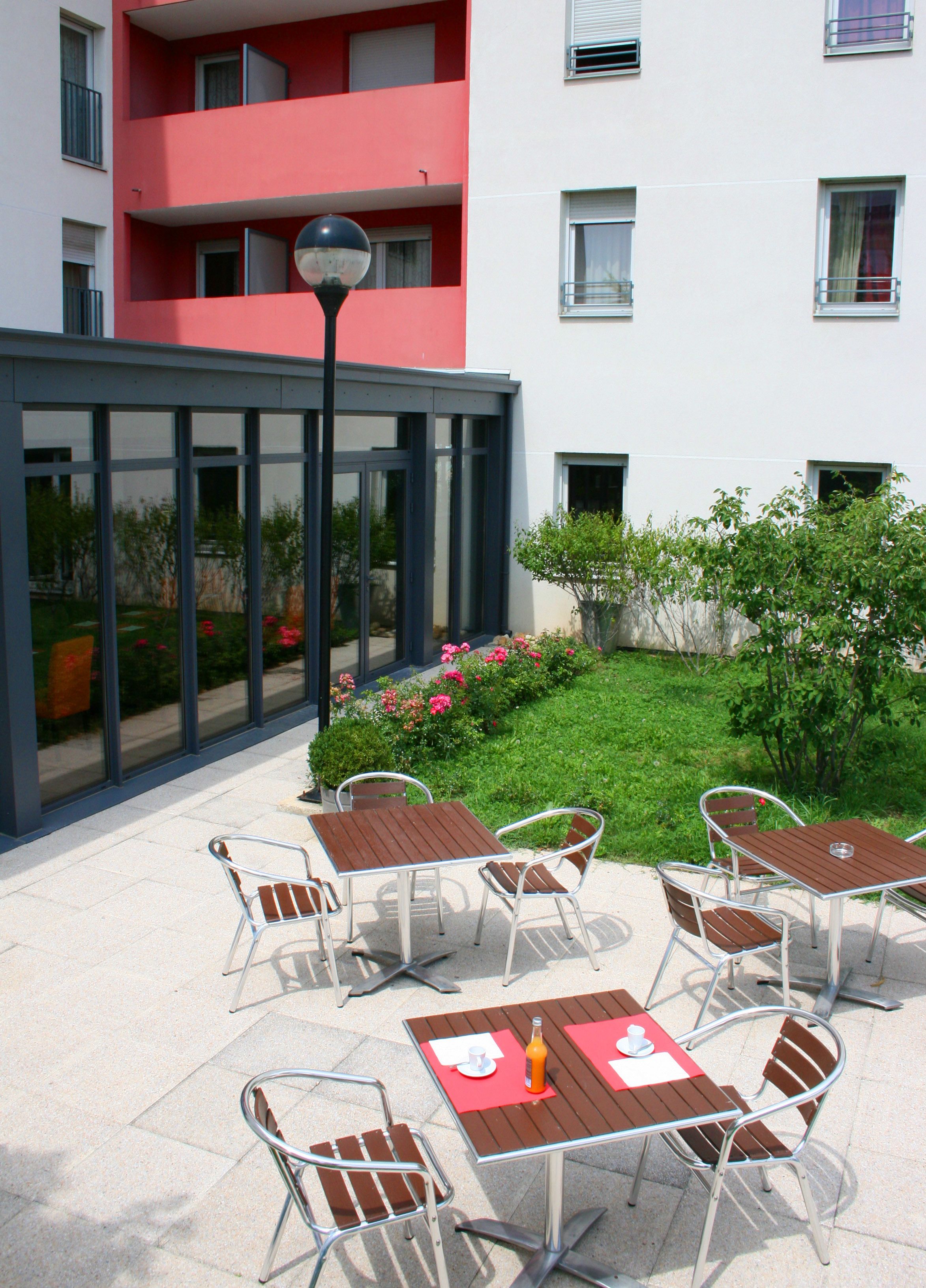 Une terrasse extérieure avec des tables et des chaises, une véranda vitrée et un jardin fleuri.