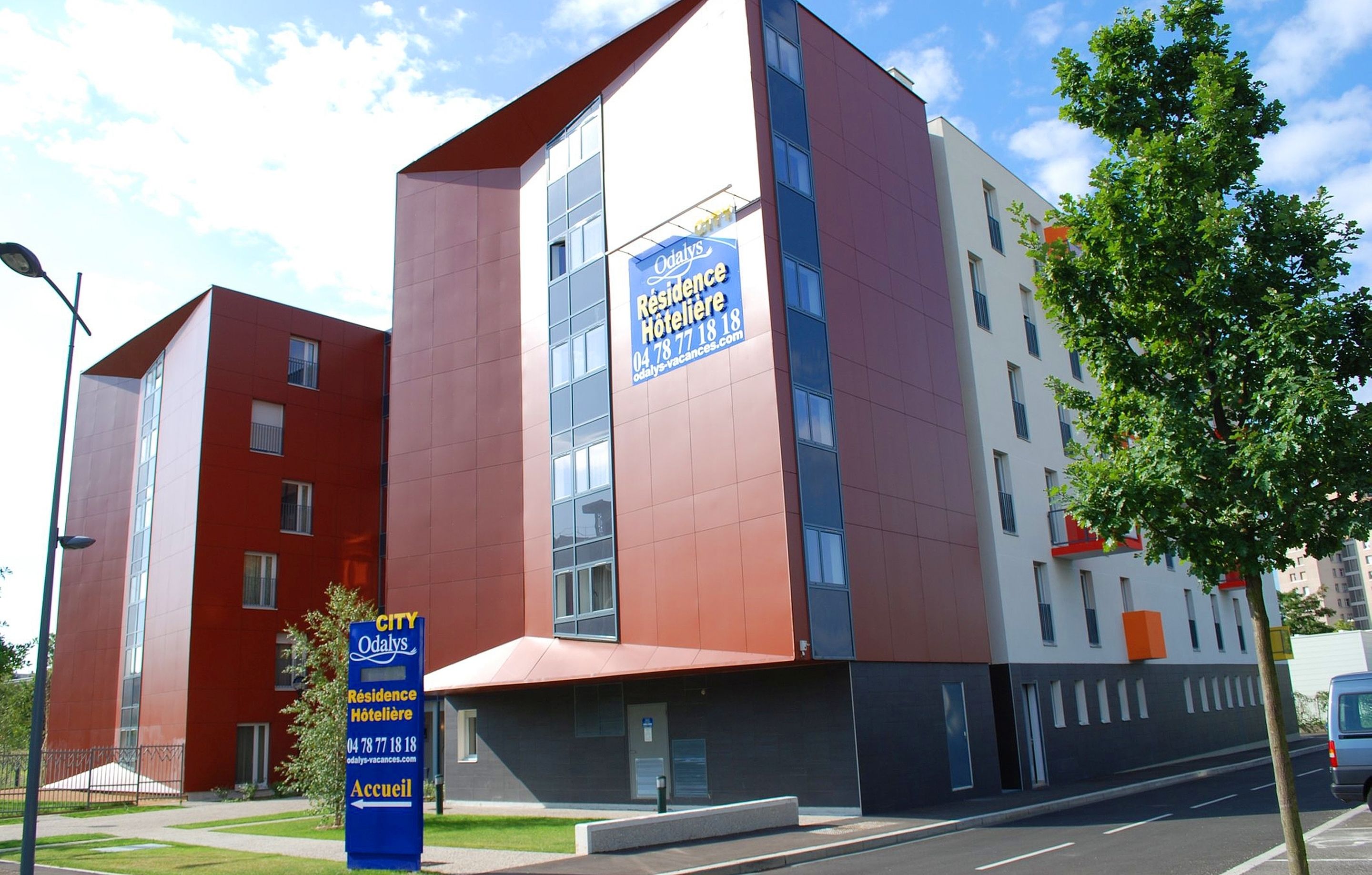 A modern hotel building with a red and white facade, large windows, and a sign indicating it is a City of Odalys hotel.